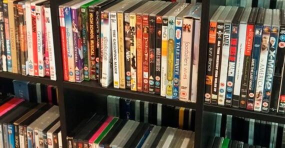A shelf filled with a collection of DVDs and Blu-rays, arranged vertically and horizontally. Various movie titles and colorful spines are visible, showing a diverse selection of films and genres.