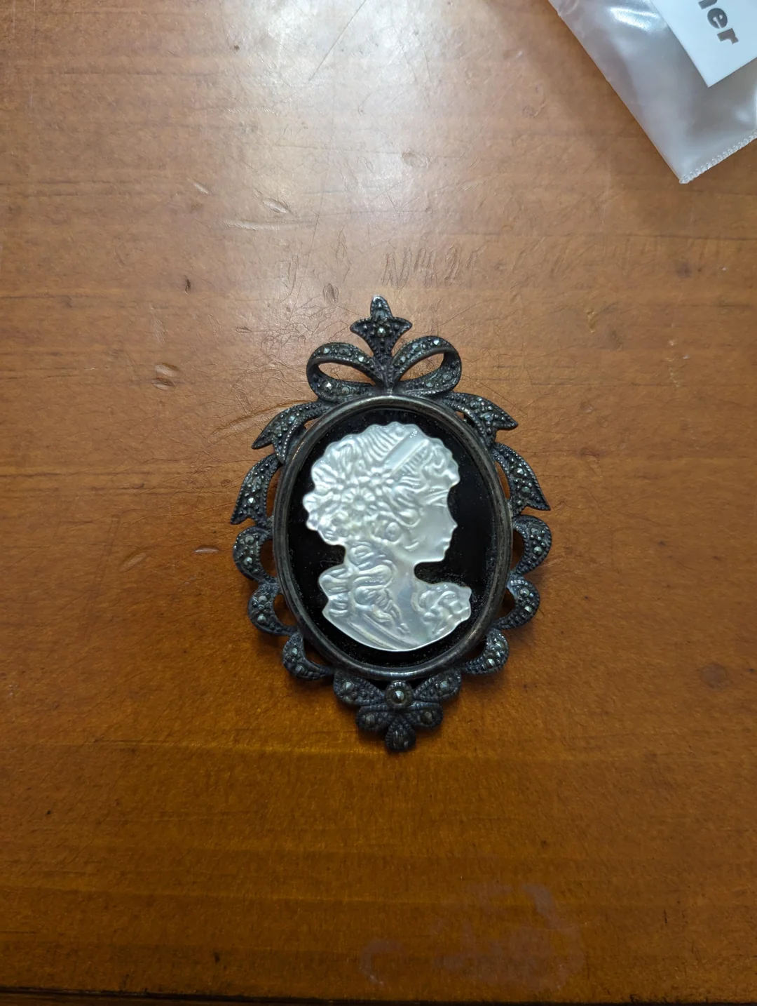 A vintage cameo brooch featuring a white profile of a woman's face with curly hair, set in an ornate dark frame, placed on a wooden surface.