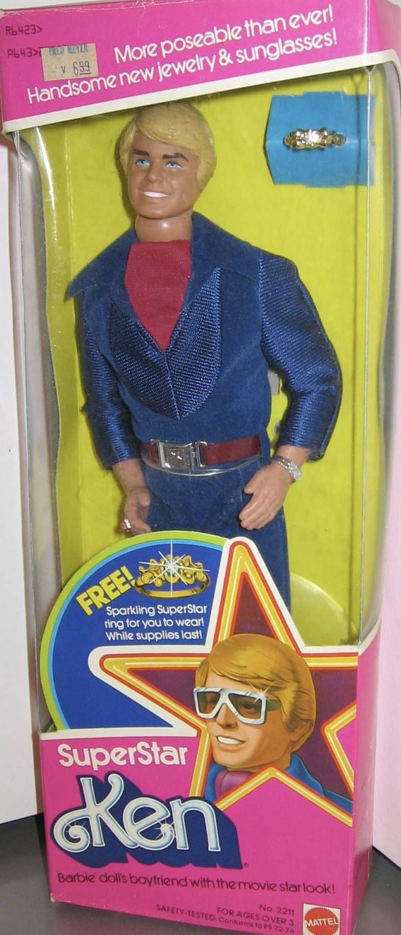 Superstar Ken doll in a blue suit with a red shirt, displayed in original Mattel packaging. The box advertises jewelry and sunglasses for Ken and features illustrated graphics of Ken wearing sunglasses.