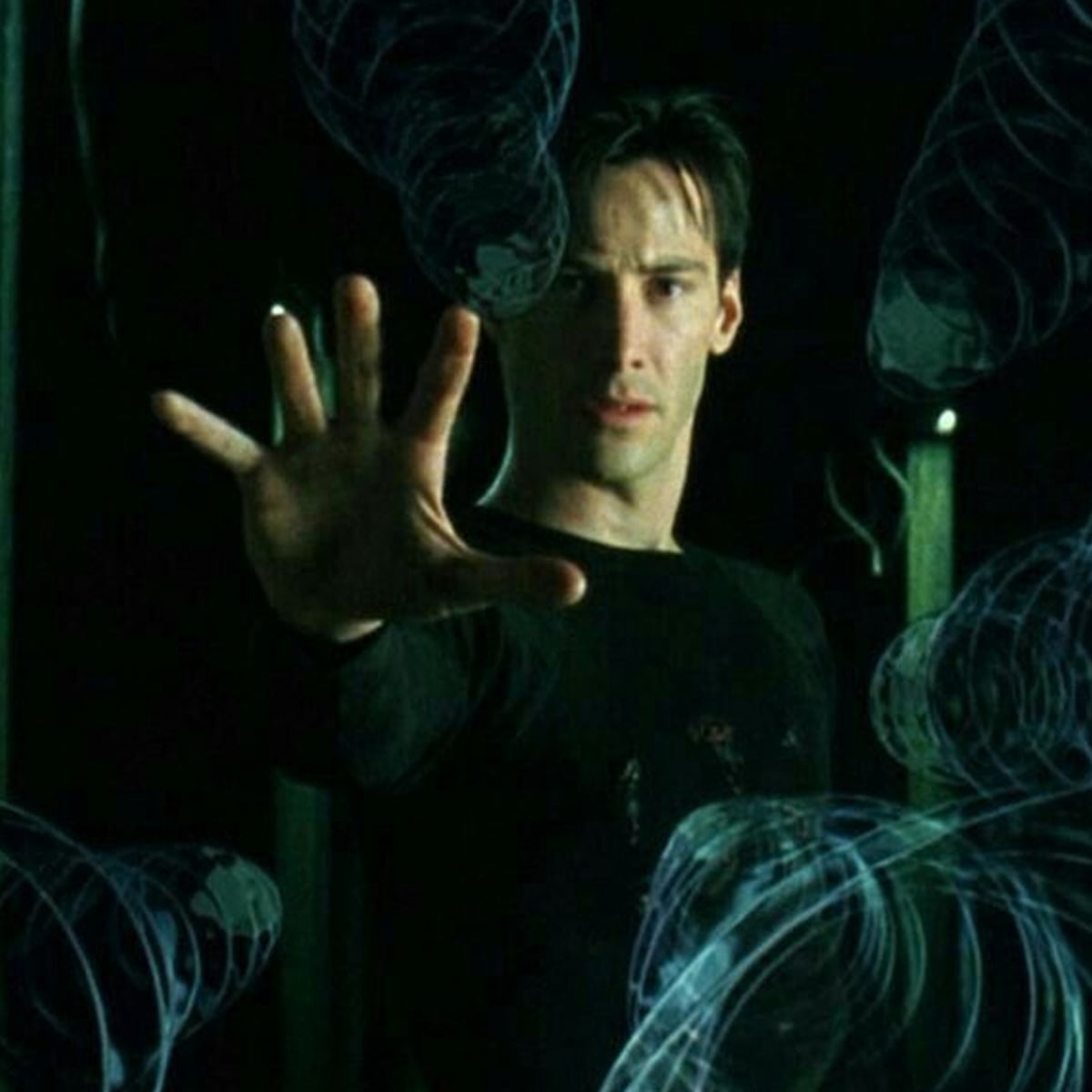 A man in a black shirt stands with his arm extended, palm out, appearing to stop or control swirling, translucent, blue-tinted objects frozen in midair around him. The scene has a dark, dramatic atmosphere.