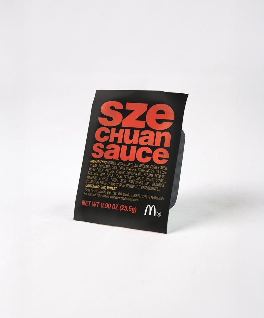 A black packet of McDonald’s Szechuan Sauce with bold red and orange text on the front, displayed against a plain white background.