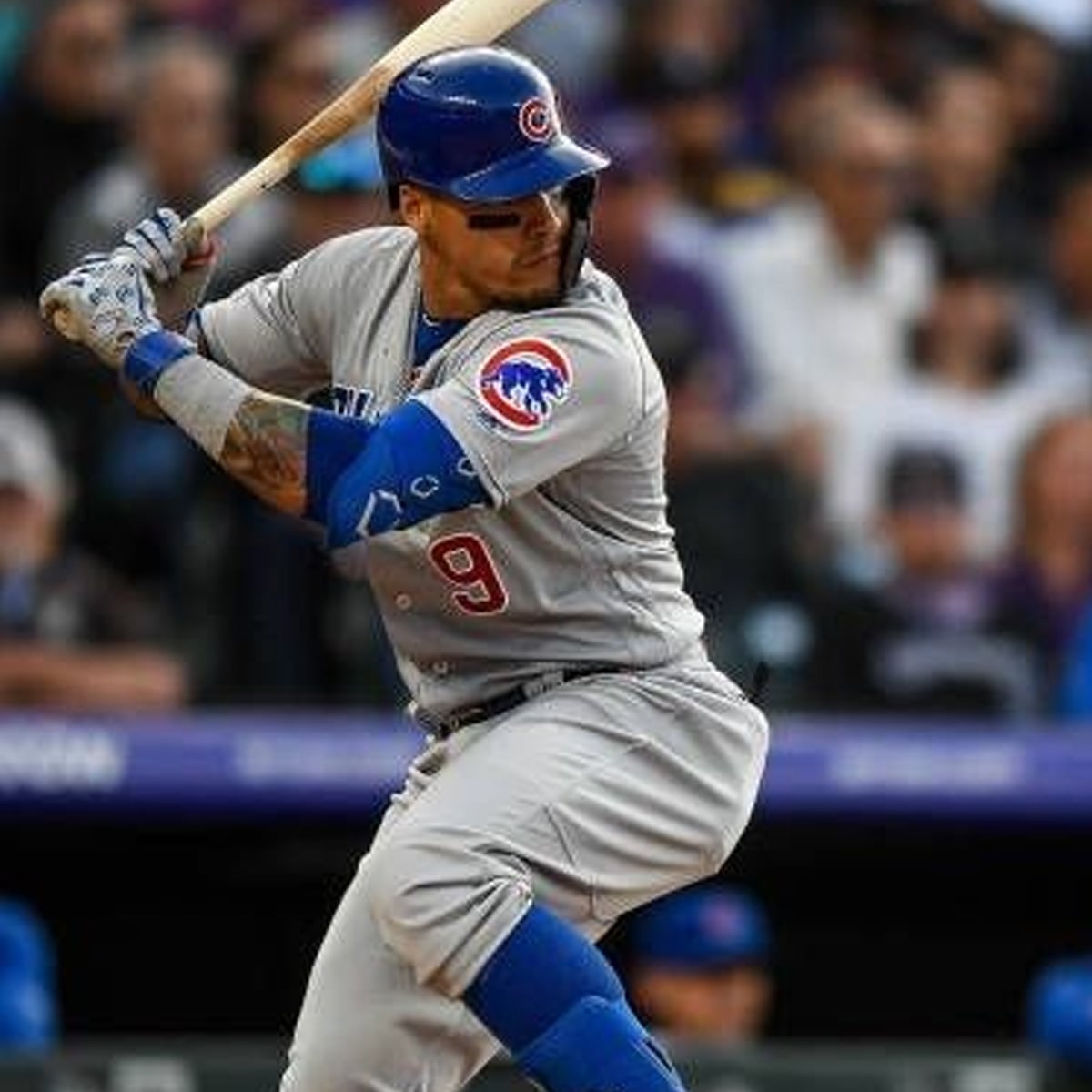 A baseball player in a gray Chicago Cubs uniform, number 9, stands at bat ready to swing during a game. The crowd is blurred in the background.