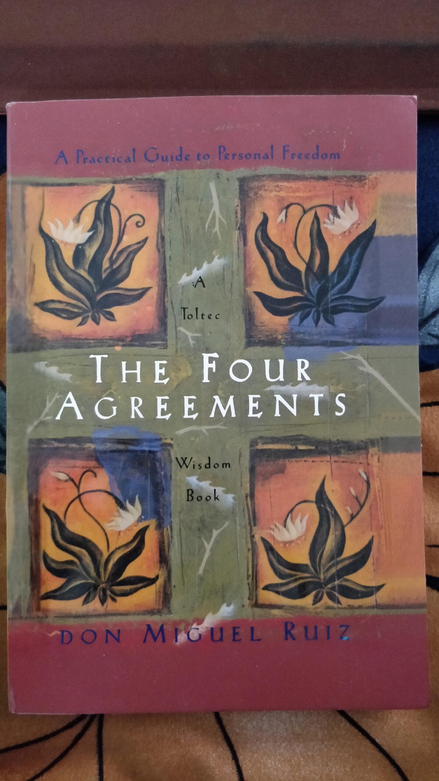 The cover of the book "The Four Agreements" by Don Miguel Ruiz features four stylized flowers and a cross pattern, with the subtitle "A Practical Guide to Personal Freedom, A Toltec Wisdom Book.