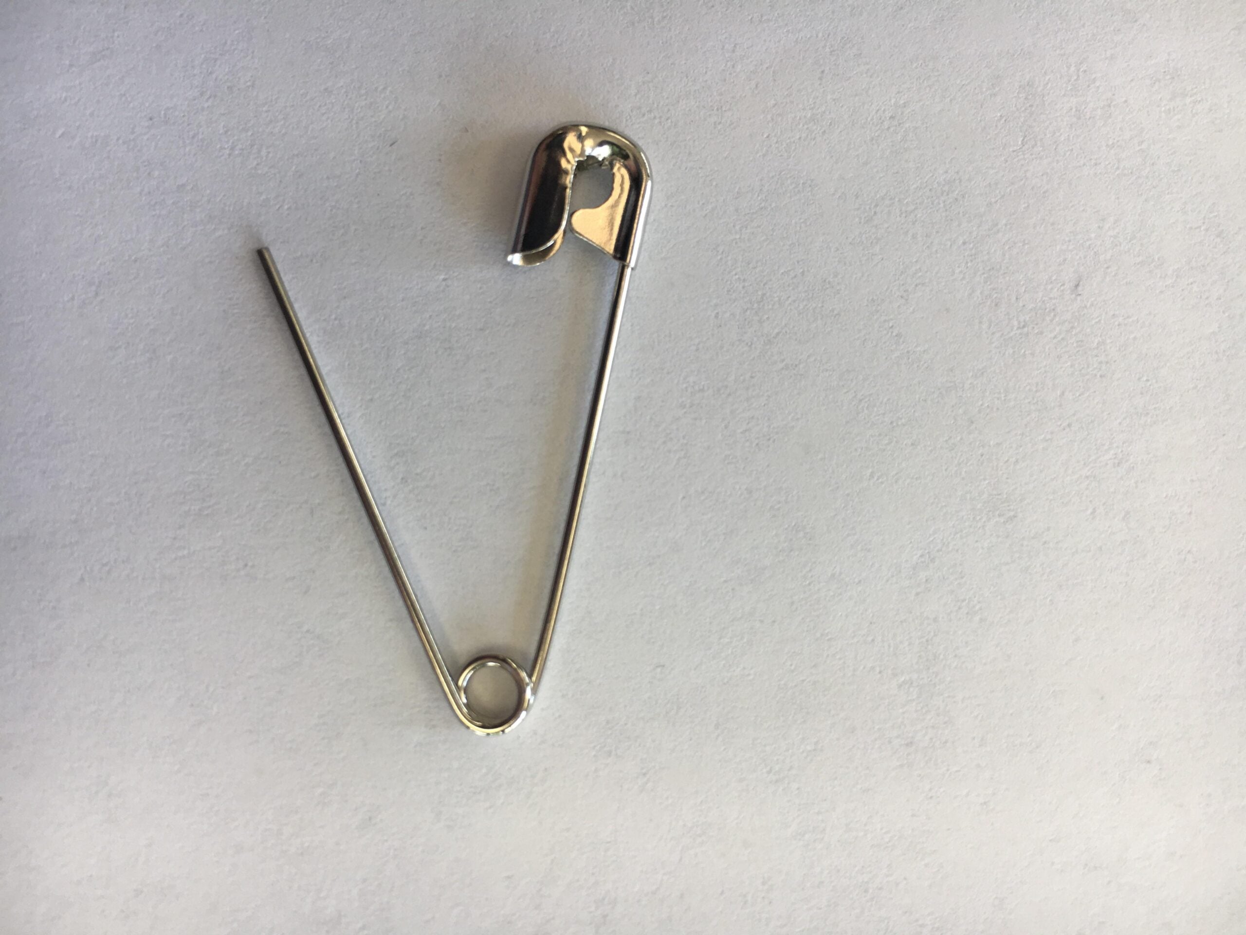 A single silver safety pin is open and lying on a plain, light-colored surface.