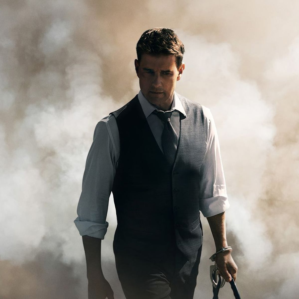 A man in a vest, dress shirt, and tie walks forward through thick clouds of smoke, holding something in his left hand, looking serious and determined.