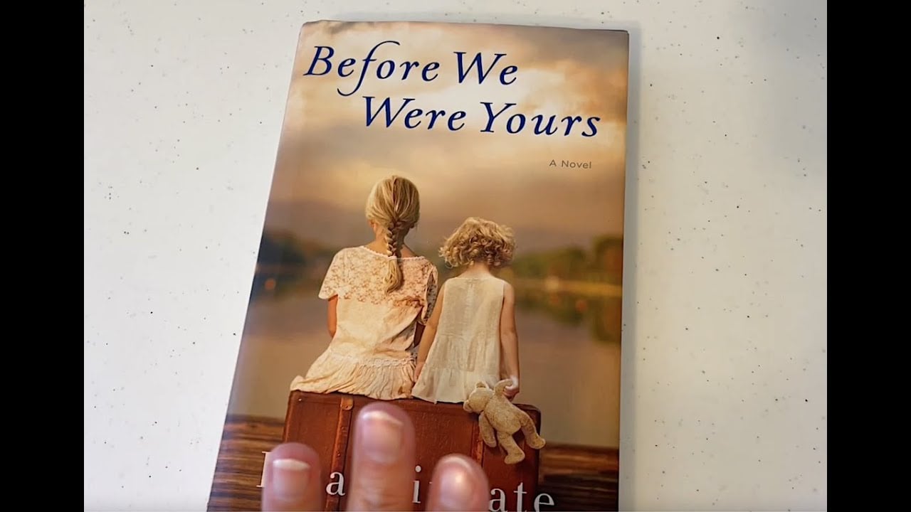 A hand holds the book "Before We Were Yours," featuring a cover image of two girls with their backs turned, sitting on a suitcase by the water, one holding a teddy bear.