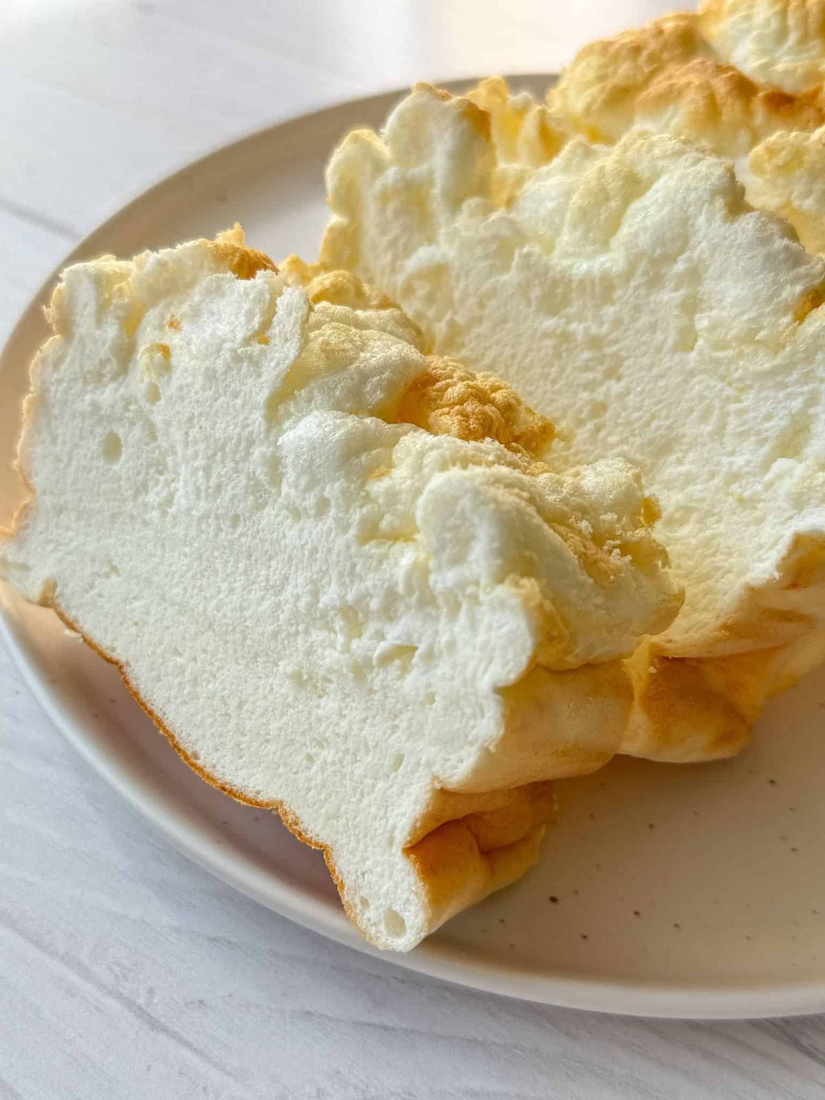 A close-up of two thick slices of fluffy, white cloud bread with a golden crust, served on a light-colored plate on a white surface.