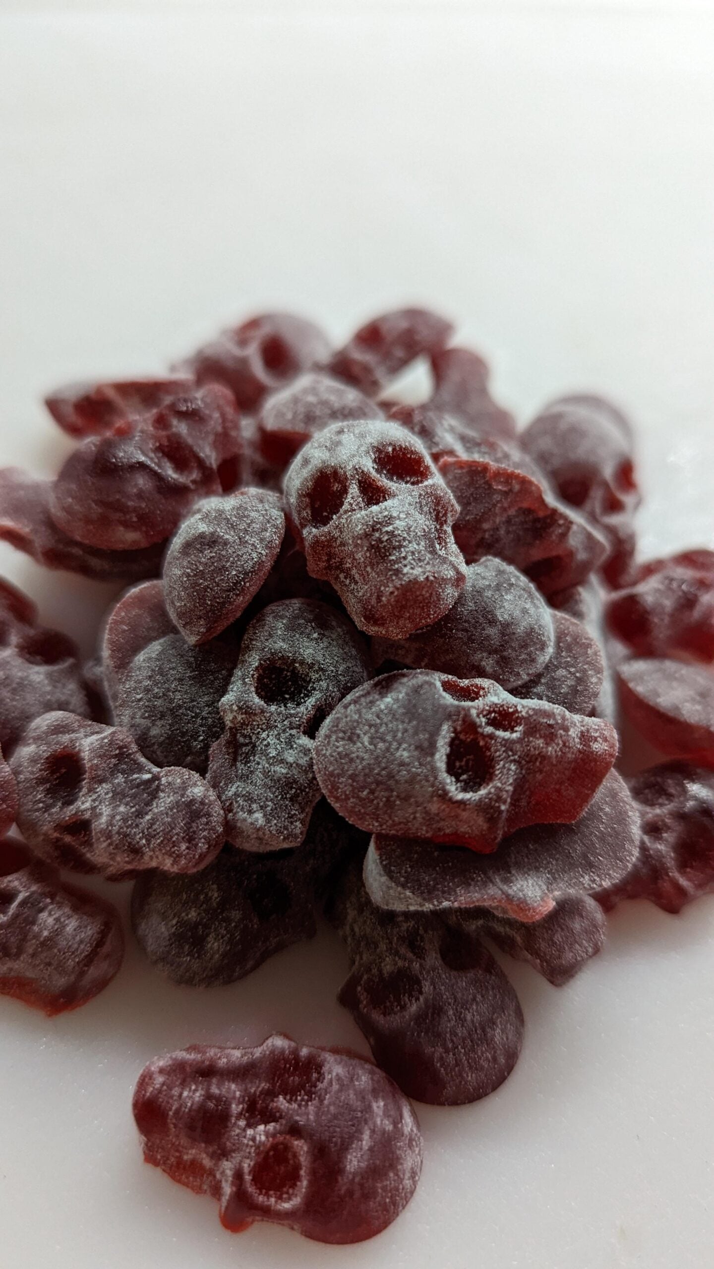 A pile of red gummy candies shaped like skulls, dusted with a light coating of white powder, on a white surface.