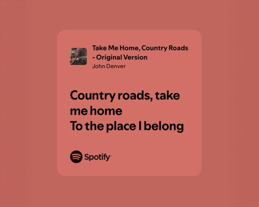 A Spotify graphic displaying “Take Me Home, Country Roads – Original Version” by John Denver. The lyrics “Country roads, take me home to the place I belong” appear in bold black text on a muted red background.