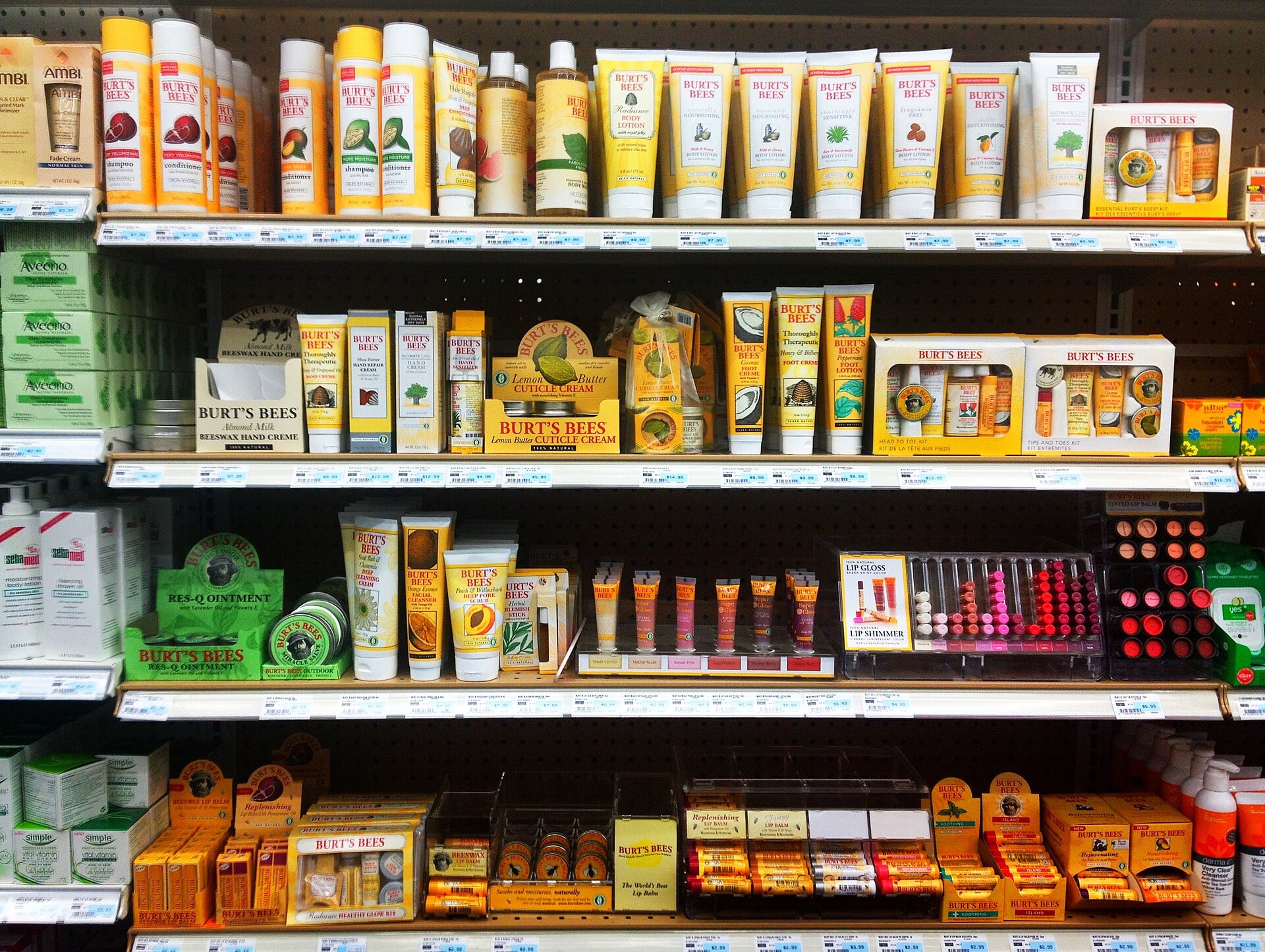 Shelves in a store display various Burt’s Bees skincare and lip balm products in yellow packaging, including lotions, creams, lip balms, and gift sets, neatly arranged in rows.