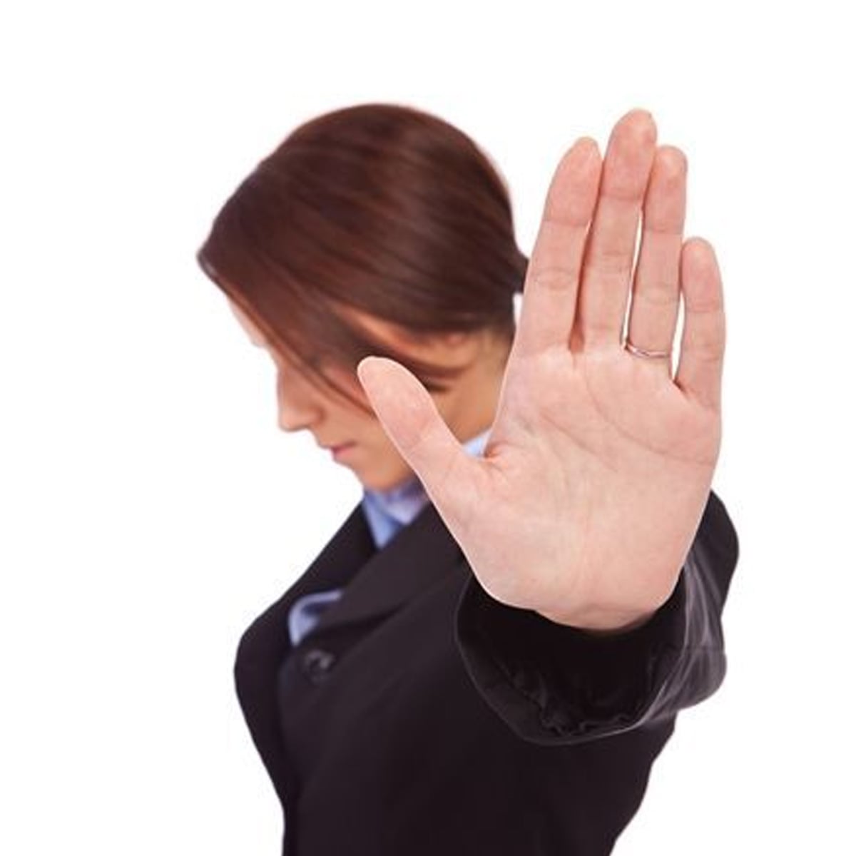 A woman in a business suit faces downward with her hand raised toward the camera in a "stop" gesture, obscuring part of her face. The background is plain white.