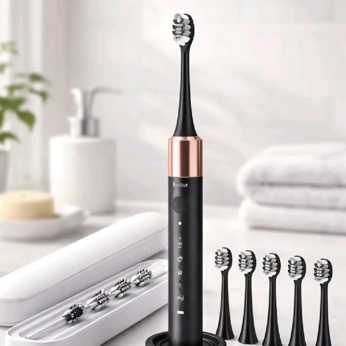 A black electric toothbrush with a rose gold accent stands upright on a bathroom counter, surrounded by six replacement brush heads and a white travel case. In the background are towels, a soap dish, and a pump bottle.