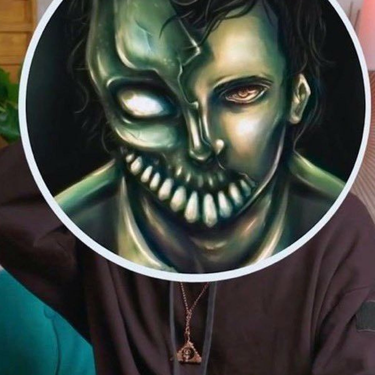 A person is holding or wearing a circular artwork over their face, showing a creepy, half-skeletal, half-human face with sharp teeth and glowing eyes. The person's body is visible, but their real face is covered.