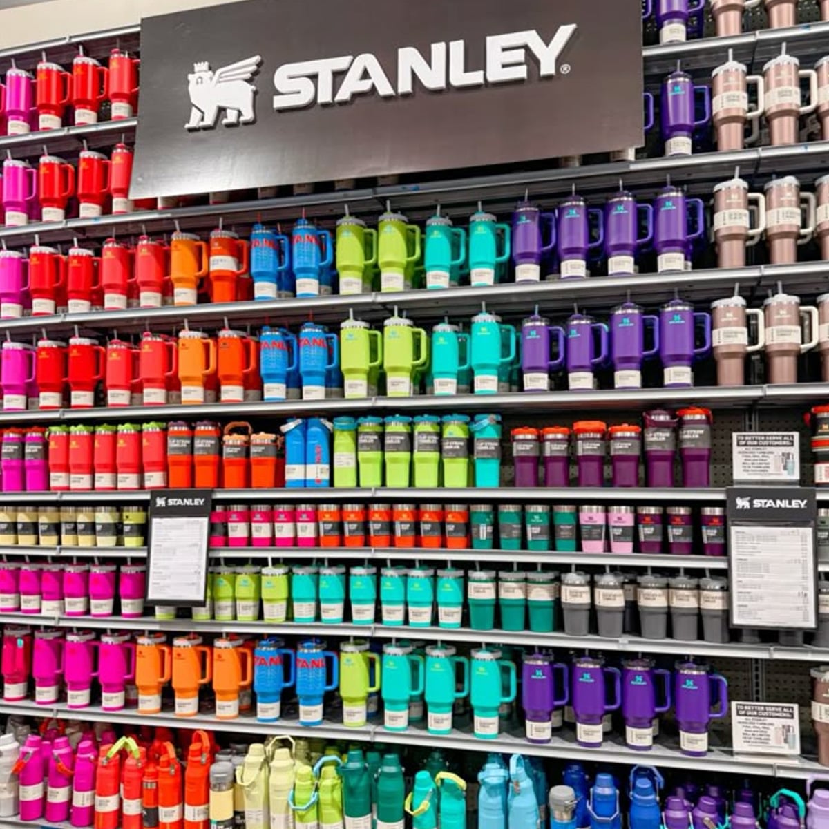 Shelves display Stanley brand insulated tumblers and bottles, neatly organized by bright colors including red, orange, yellow, green, blue, and purple, beneath a prominent Stanley sign in a retail store.