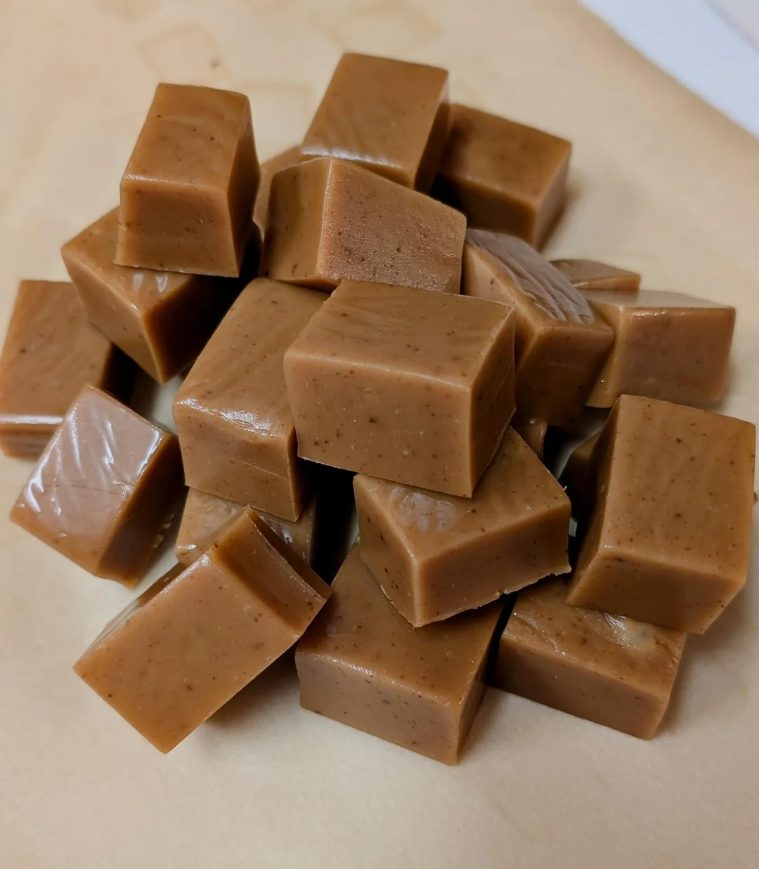 A pile of rectangular, brown caramel candies stacked on a light surface. The candies have smooth, glossy surfaces and sharp edges, indicating they are freshly made or cut.