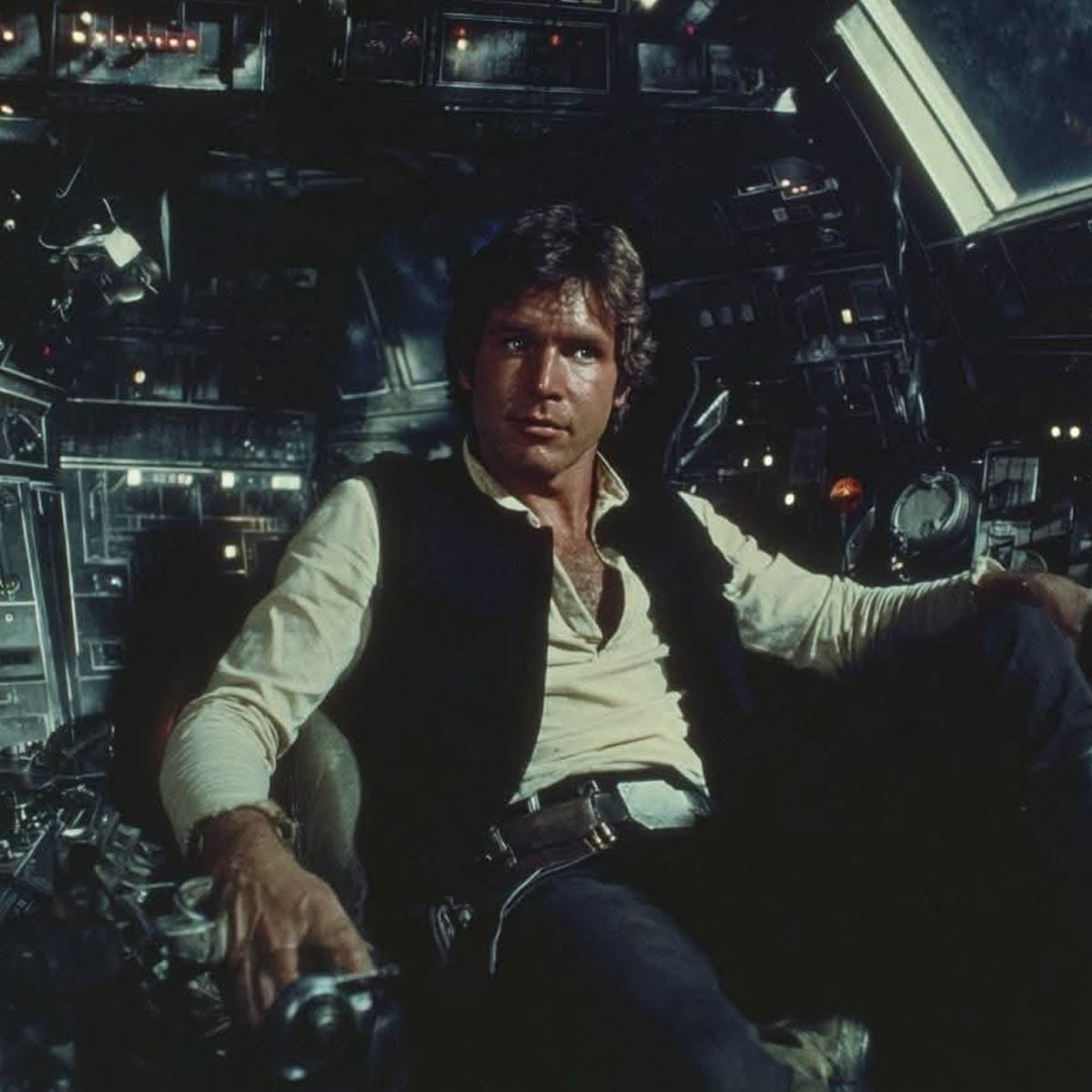 A man with brown hair and a vest sits in the cockpit of a spaceship, surrounded by illuminated control panels and buttons.