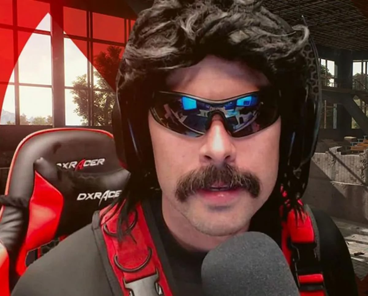 A man with a black wig, sunglasses, and a thick mustache speaks into a microphone. He wears a red and black headset and sits in a gaming chair, with a dramatic red-lit background behind him.
