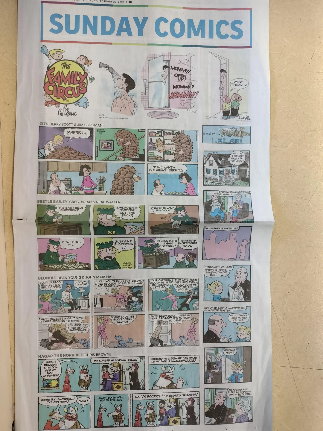 A newspaper page titled "Sunday Comics" displays several colorful comic strips, including The Family Circus, Beetle Bailey, Blondie, Hägar the Horrible, and others, arranged in horizontal rows.