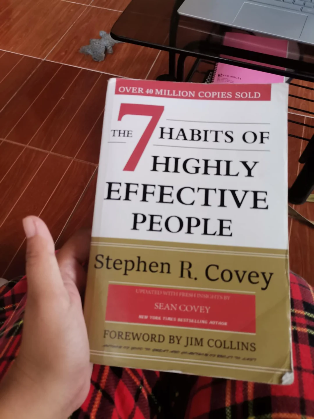 A hand holds the book "The 7 Habits of Highly Effective People" by Stephen R. Covey. The cover also mentions a foreword by Jim Collins and says over 40 million copies have been sold.