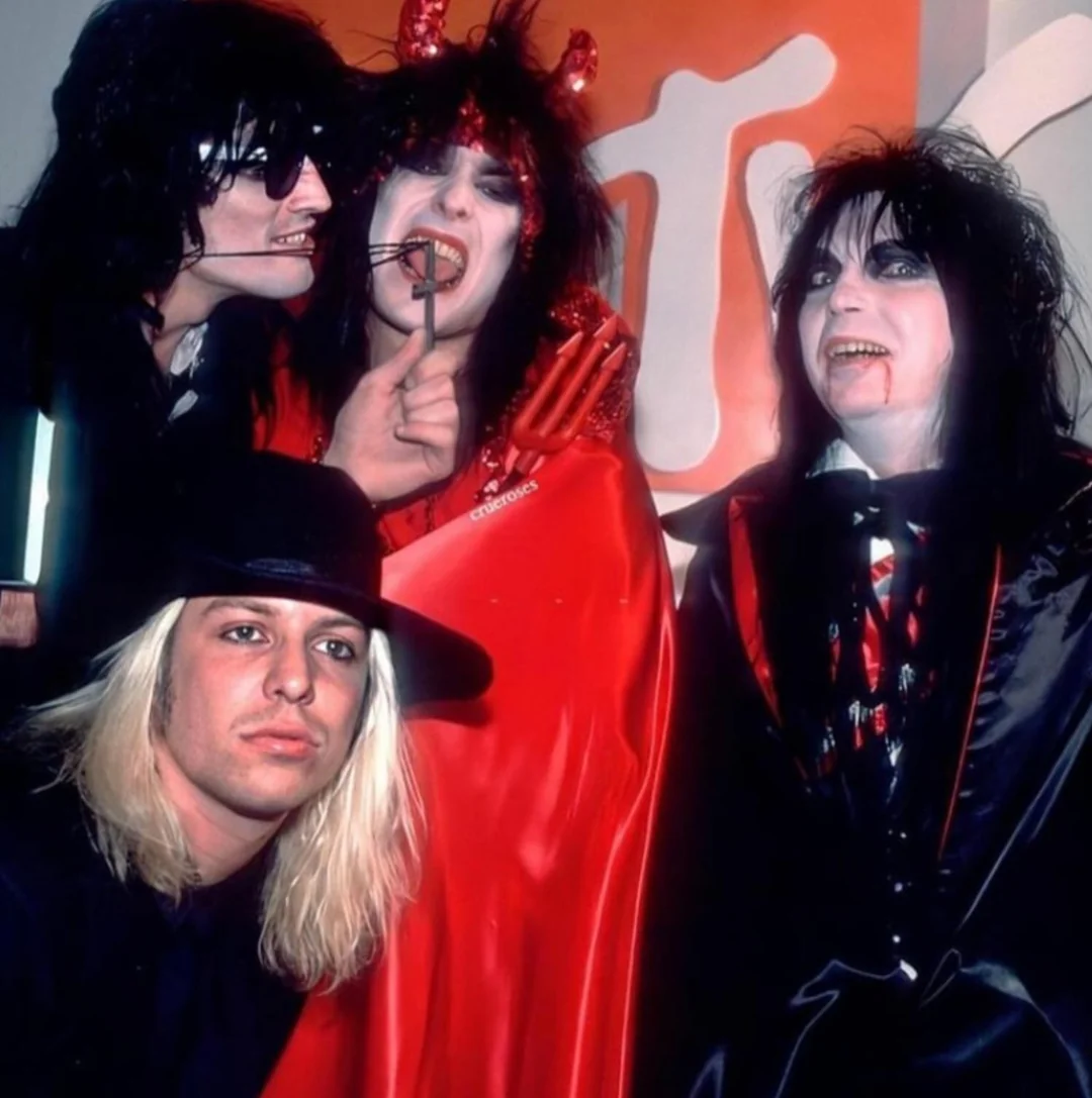 Four people dressed in dramatic Halloween costumes pose together; one wears a hat and has long blond hair, two have ghostly makeup and dark hair, and one is dressed as a devil with red horns, red cape, and a forked prop. MTV logo in background.