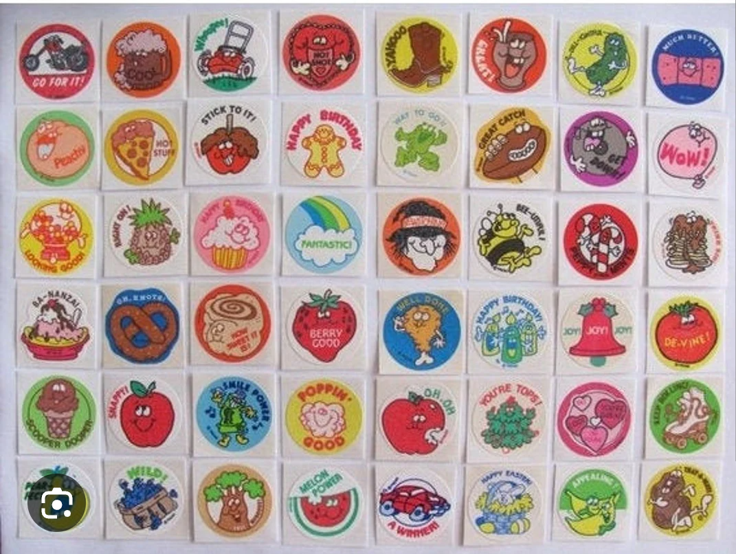 A grid of colorful vintage scratch-and-sniff stickers featuring cartoon food, animals, and positive messages like "Go For It!", "Fantastic", and "Poppin'!" against a white background.
