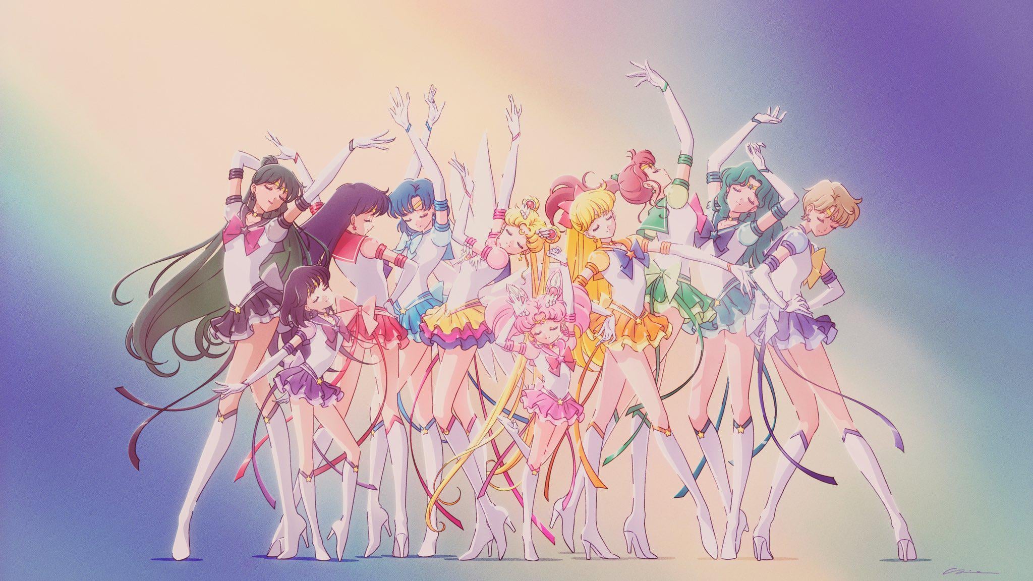 Nine animated girls in colorful sailor-inspired outfits pose together with outstretched arms against a soft pastel background, evoking an energetic and heroic atmosphere.