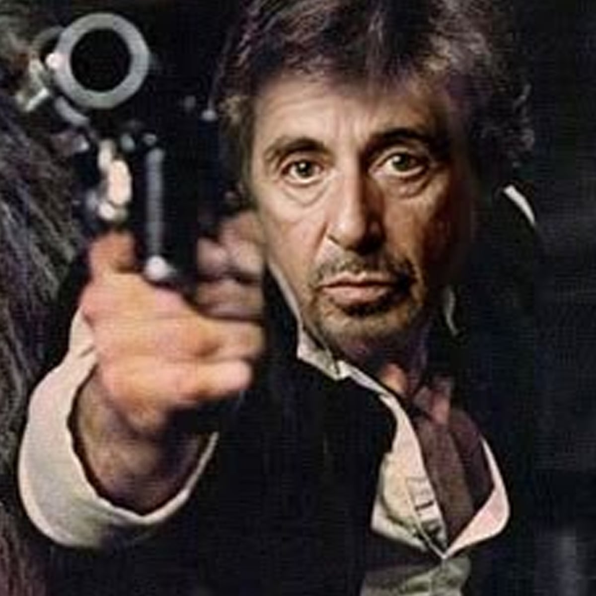 A man with dark hair and intense expression points a handgun directly at the camera, wearing a partially unbuttoned shirt and a vest, with a blurred background behind him.