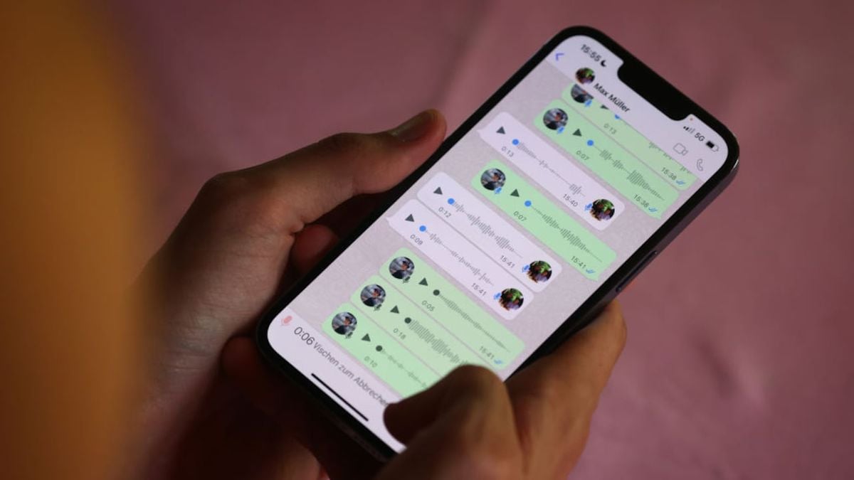A person holding a smartphone with a WhatsApp chat open, showing multiple voice messages exchanged in a conversation. The background is slightly blurred.