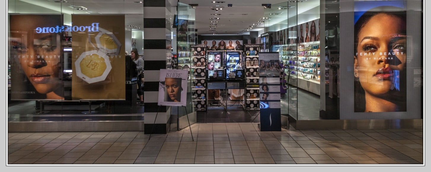 A makeup store with large Fenty Beauty ads featuring models’ faces, bright lighting, and shelves stocked with cosmetics; the entrance is open, inviting shoppers inside.