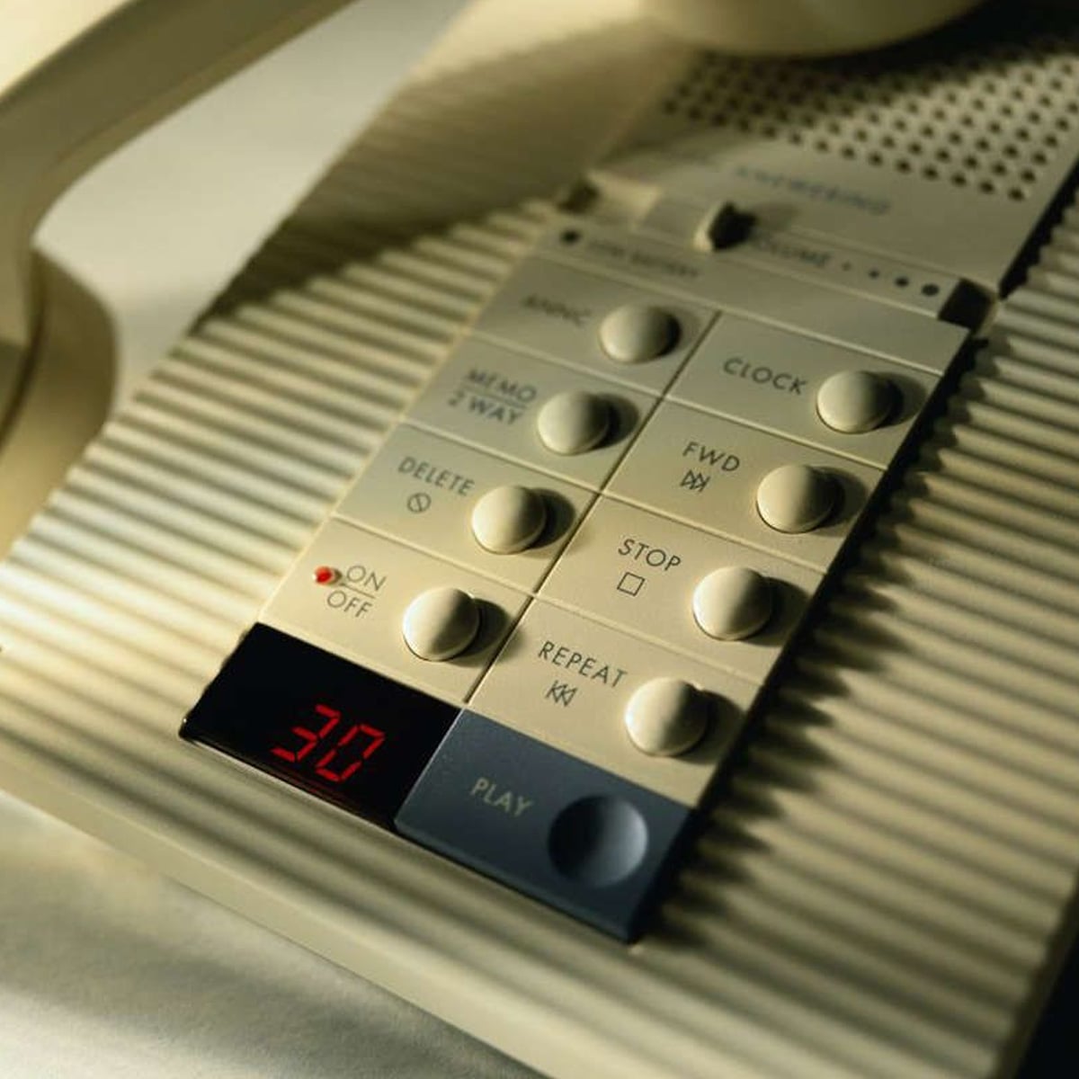 Close-up of a beige answering machine with various buttons labeled Memo, Clock, Delete, Stop, Play, and Repeat. A small red LED display shows the number 31, and the device is set to "On.