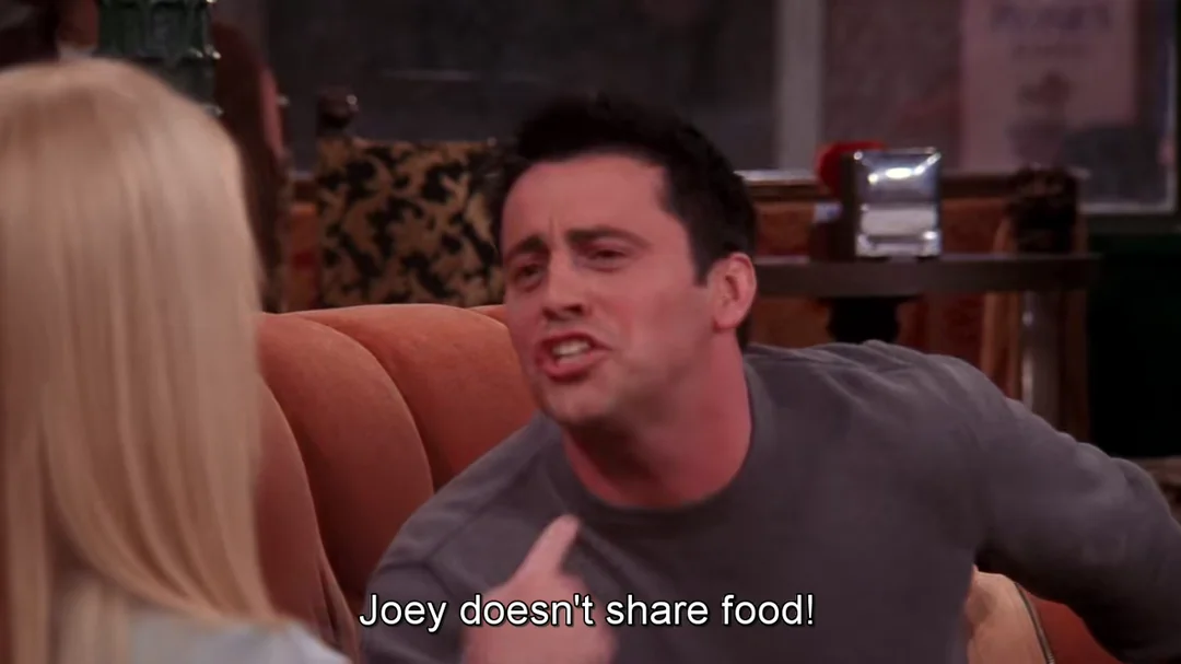 A man sitting on an orange couch angrily gestures and says, "Joey doesn't share food!" to a blonde woman, as seen in the subtitles. The setting appears to be a coffee shop.