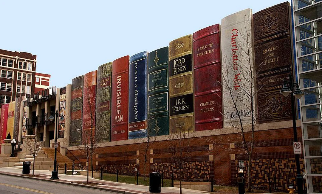 A building facade designed to look like a row of giant upright books with famous titles, including "The Lord of the Rings" and "To Kill a Mockingbird," along a city street.