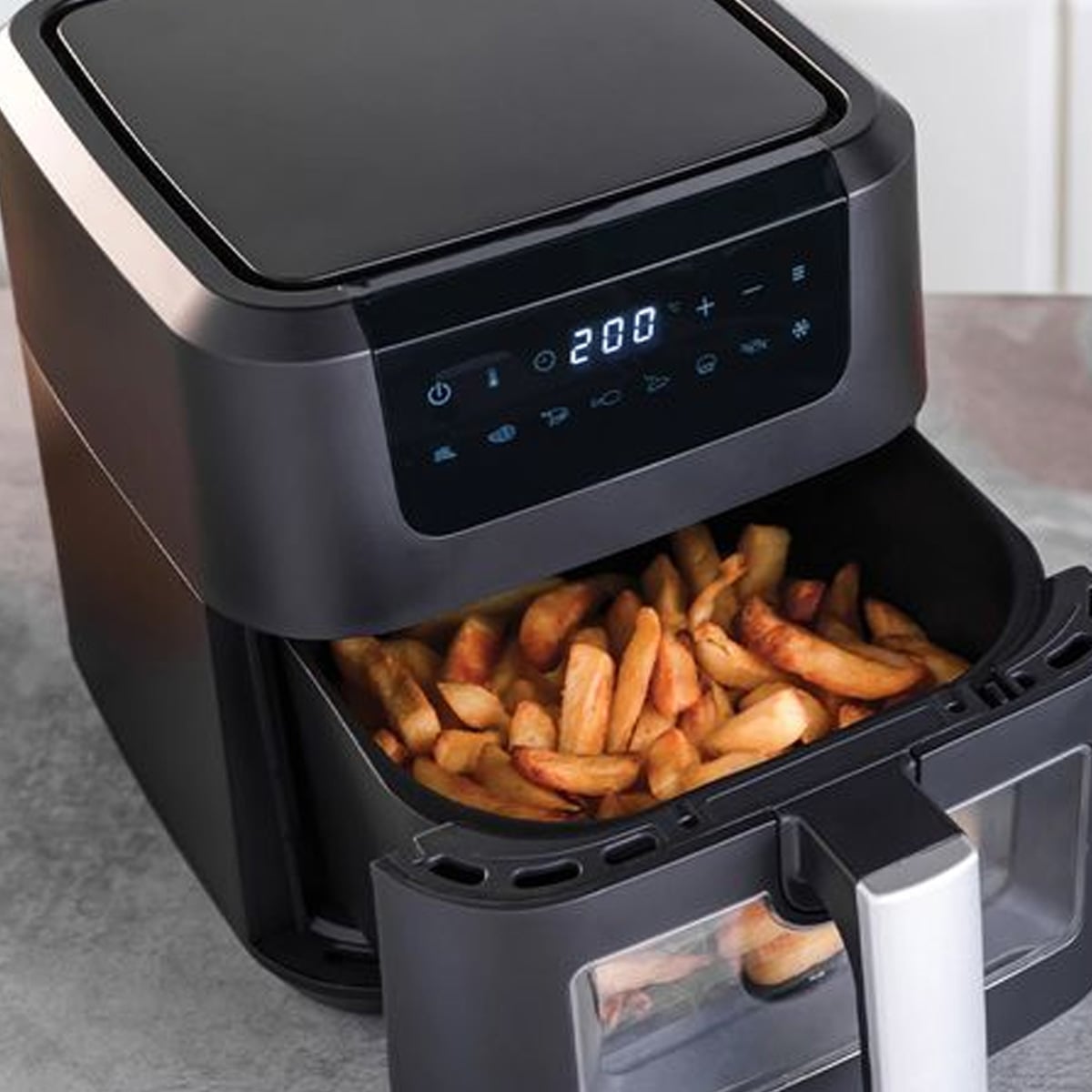A black air fryer with a digital display set to 200°C sits on a countertop, with its drawer open to reveal a batch of cooked French fries inside.