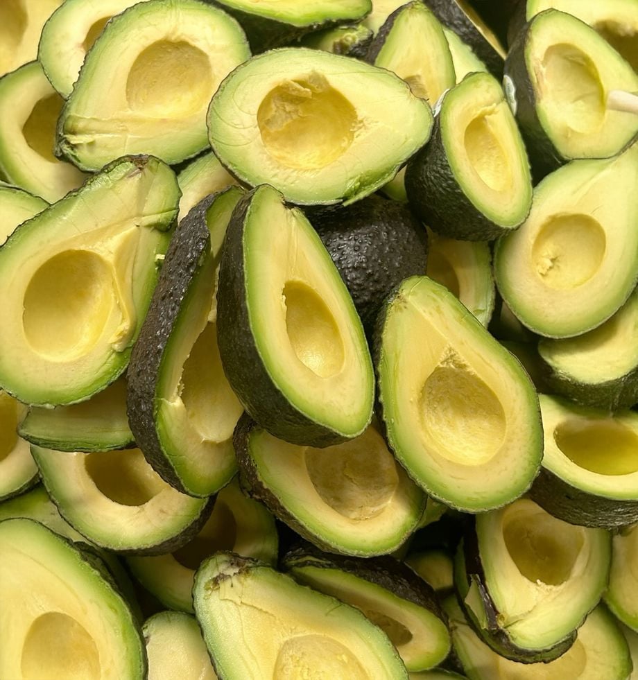 A pile of halved avocados with the pits removed, showing their creamy yellow-green flesh and dark green skins.