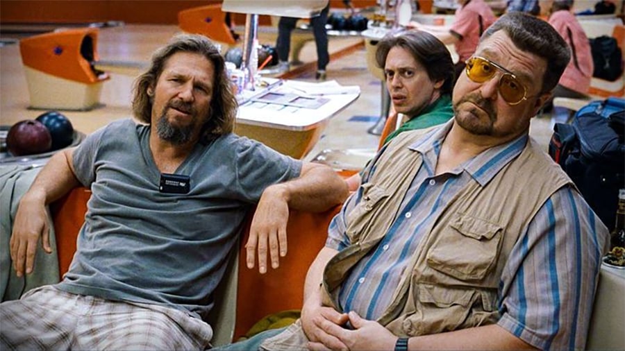Three men sit together in a retro bowling alley; one wears a gray shirt and looks relaxed, another in the middle looks surprised, and the third wears tinted glasses and a vest, gazing seriously at the camera. Bowling balls are visible behind them.