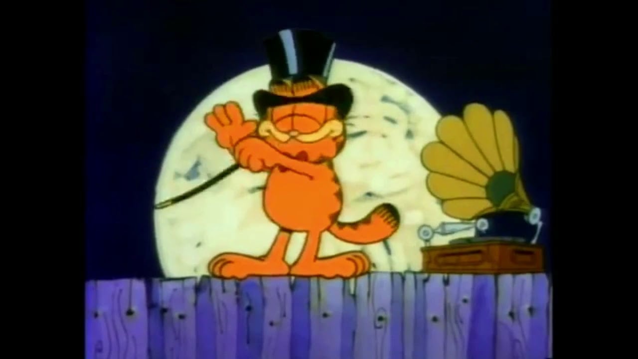 Garfield, wearing a black top hat and holding a cane, stands on a wooden fence in front of a full moon. A vintage gramophone sits nearby, and Garfield appears to be performing or dancing.
