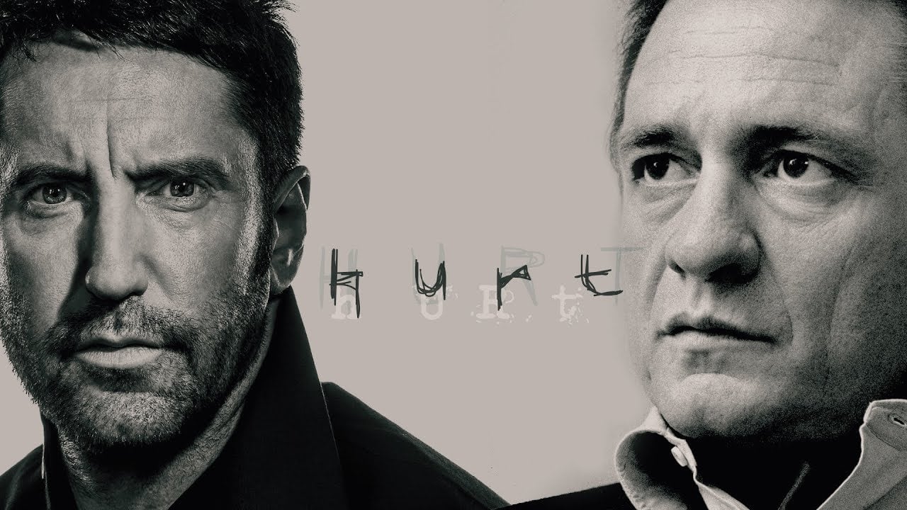 Black and white photo of two serious-looking men facing slightly toward each other. The word "HURT" appears in stylized text between them against a light background.