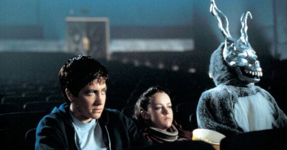 A young man, a young woman, and a person in a creepy rabbit costume sit together in an otherwise empty movie theater, looking ahead with serious expressions.
