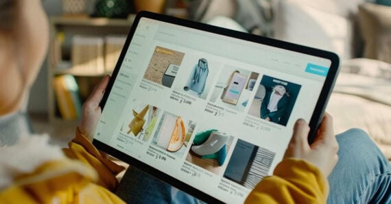 A person holding a tablet and browsing an online shopping website displaying various products, including clothes, electronics, and home decor items.