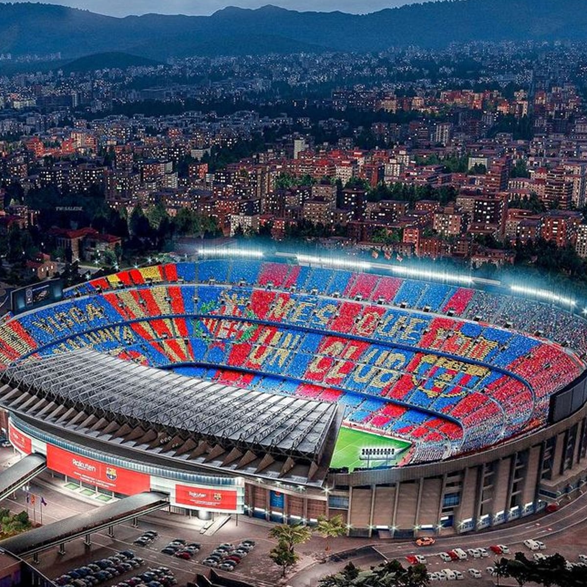 Aerial view of a brightly lit football stadium filled with fans creating a colorful mosaic with red, blue, and yellow cards. The surrounding city and hills are visible at dusk.