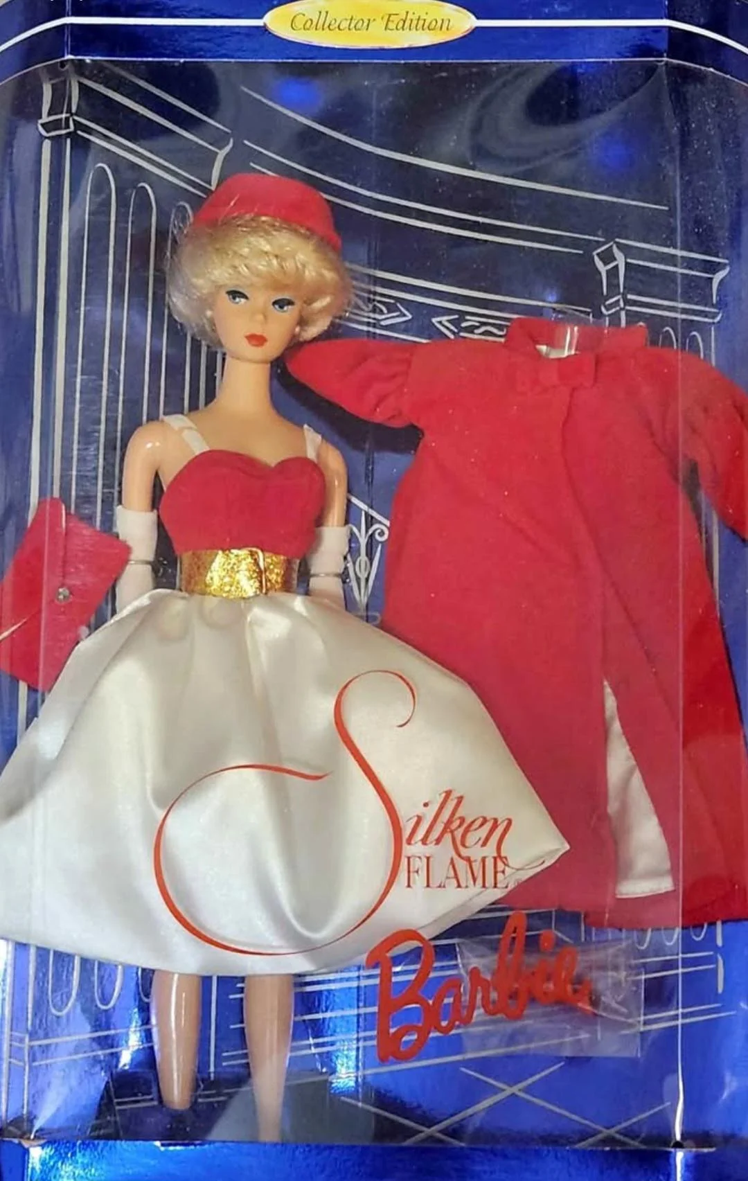 Barbie doll in a collector edition box, wearing a white and red dress with a gold belt, red hat, and gloves. A matching red coat and purse are displayed beside her. "Silken Flame Barbie" is written on the box.