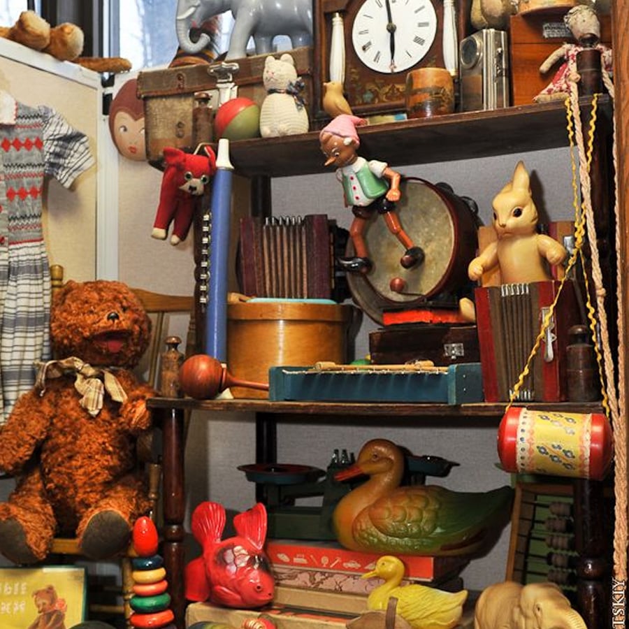 Shelves filled with vintage toys, including a teddy bear, toy duck, drum, stuffed animals, books, a clock, and various colorful collectibles, creating a nostalgic scene.