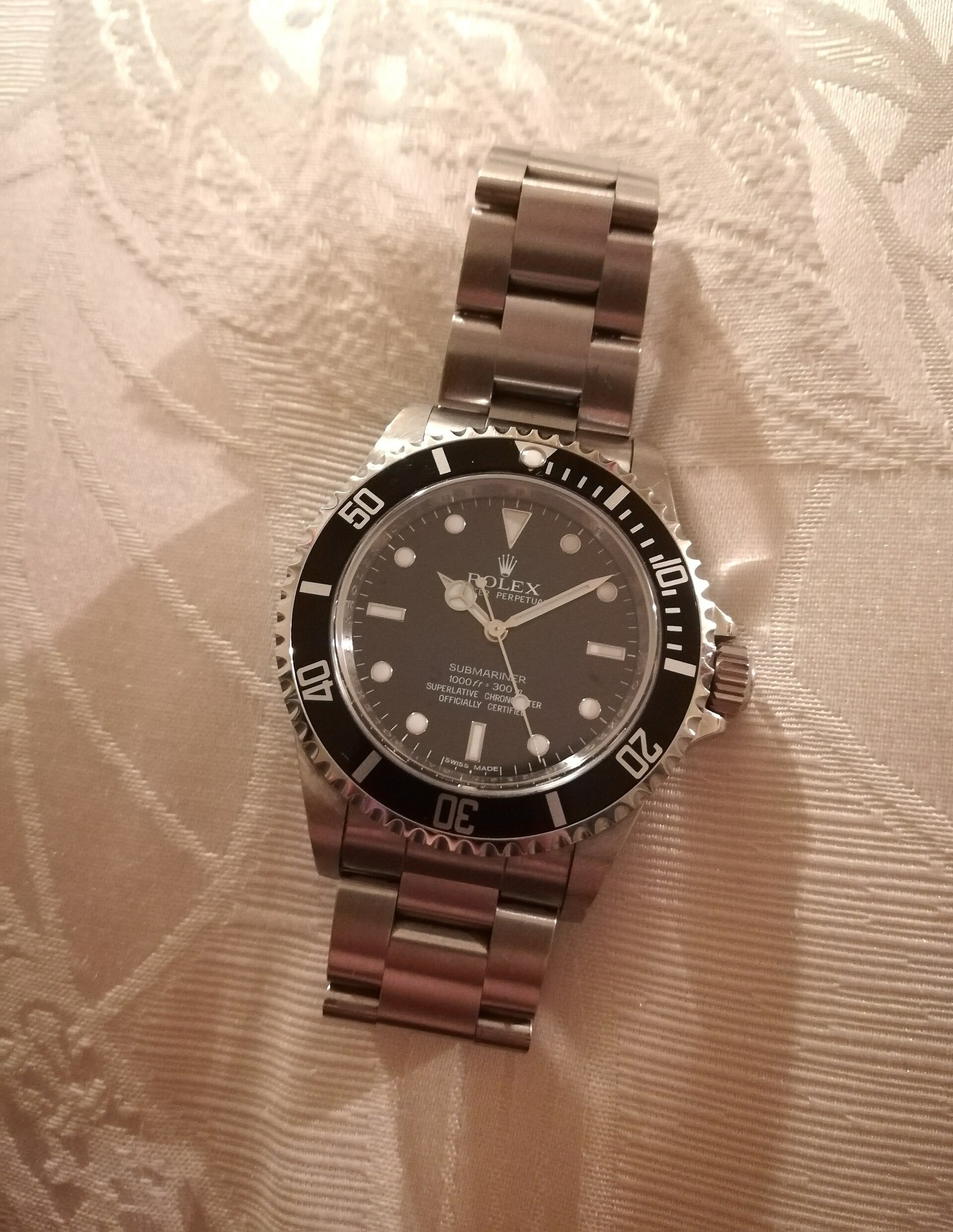 A stainless steel Rolex Submariner watch with a black dial and bezel is placed on a textured, light-colored fabric surface.