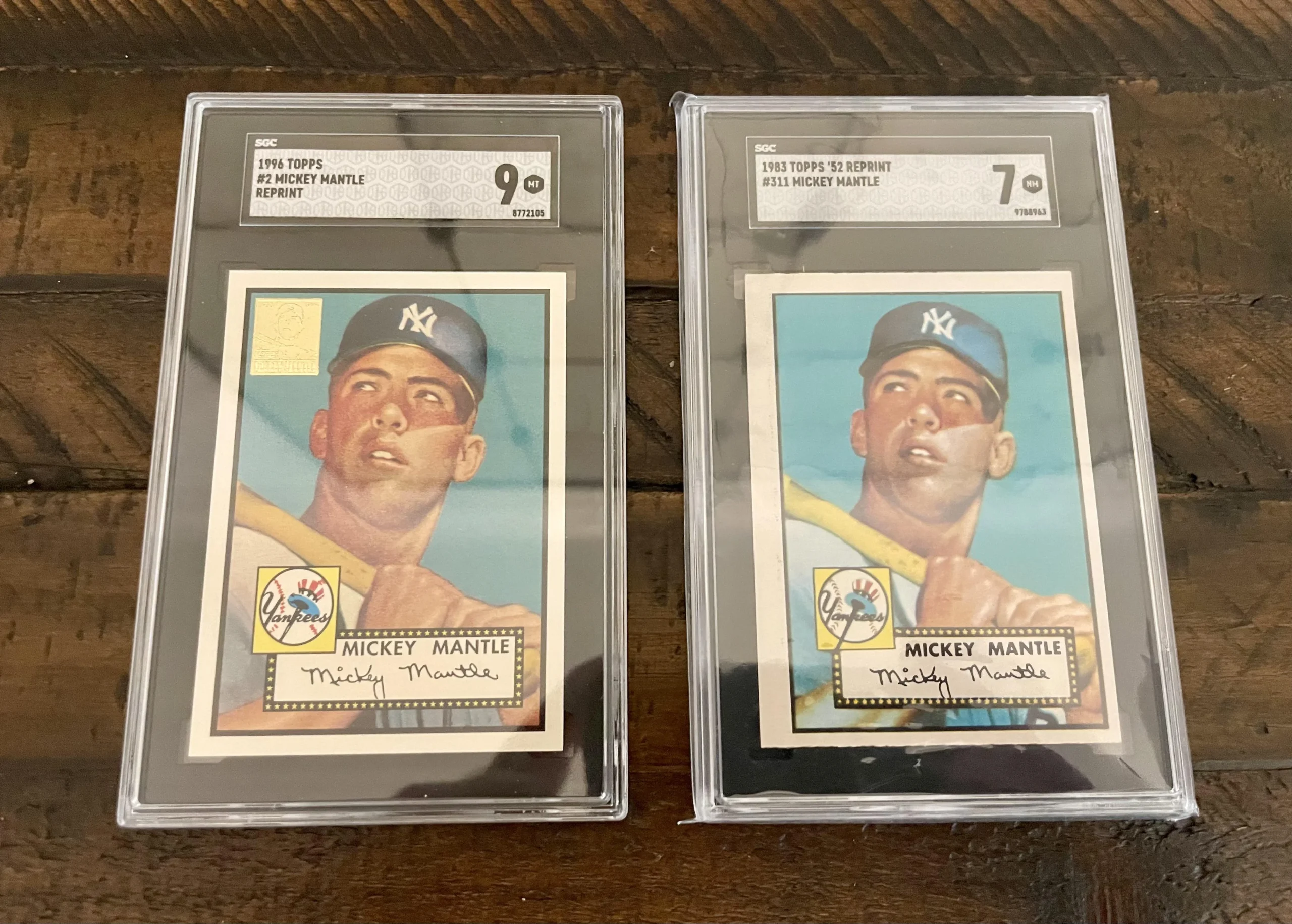 Two graded 1952 Topps Mickey Mantle baseball cards in protective cases, displayed side by side on a wooden surface. The left card is graded 9, the right card is graded 7.