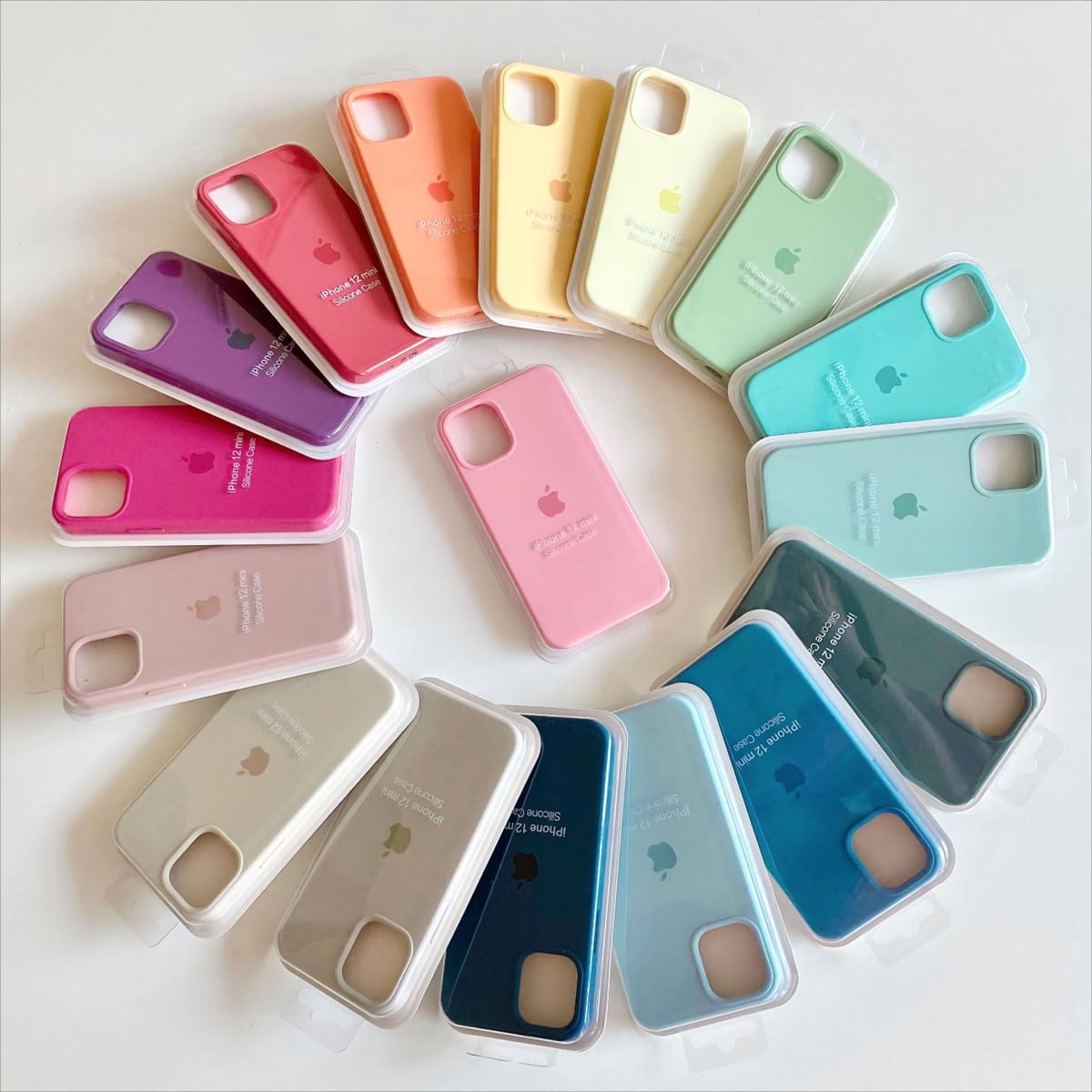A spiral arrangement of iPhone cases in various colors, including pink, orange, yellow, green, blue, and beige, displayed on a white surface. Each case is in its packaging with the Apple logo visible.