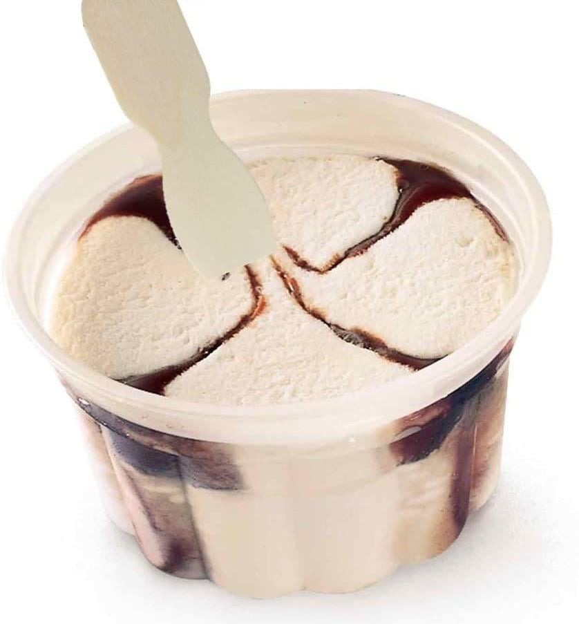 A small plastic cup of vanilla ice cream with chocolate syrup swirls forms a clover shape on top. A wooden spoon is inserted into the ice cream.