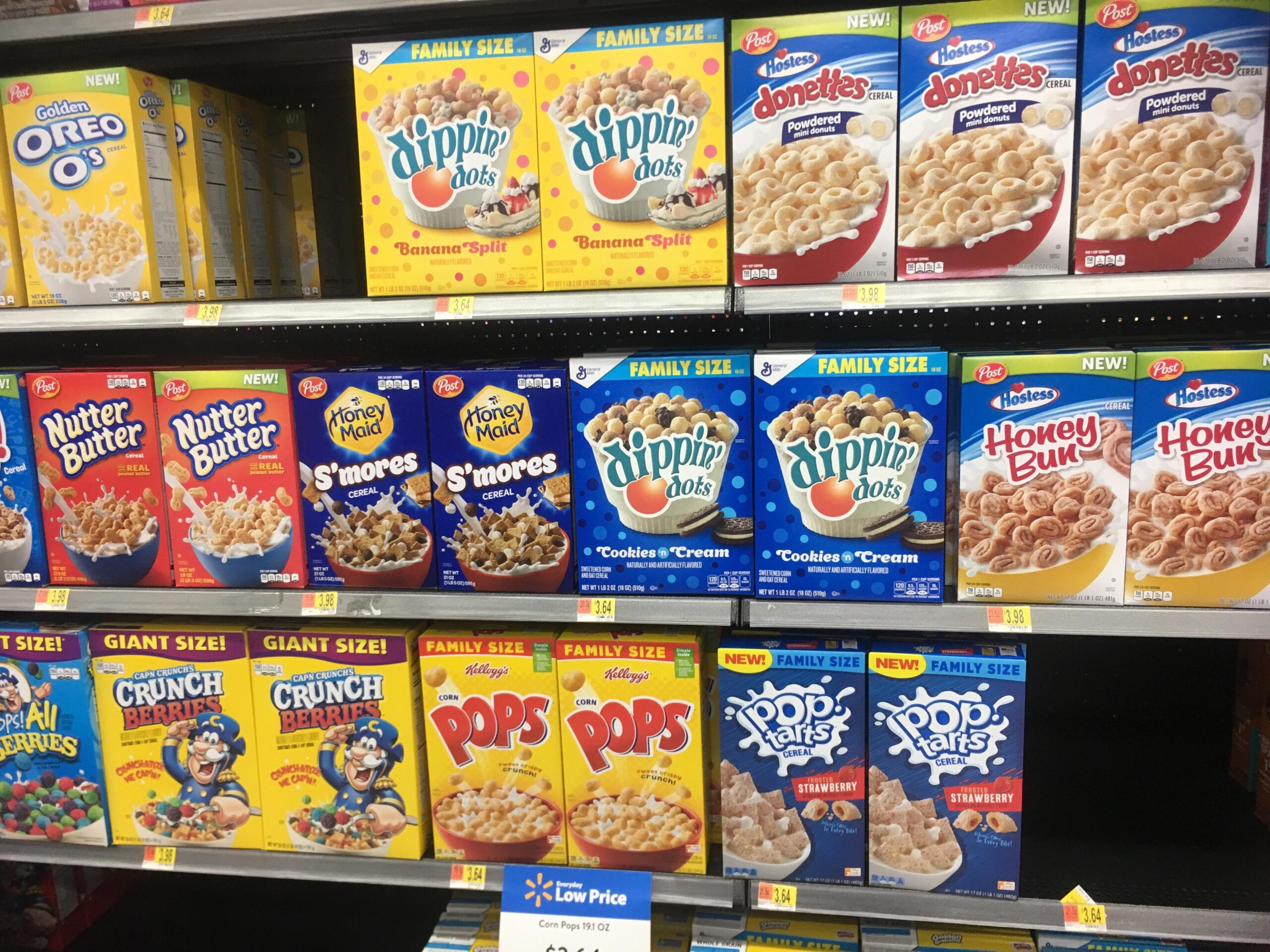 Shelves stocked with various family-size cereals, including Oreo O’s, Dippin’ Dots, Donettes, Nutter Butter, S’mores, Honey Bun, Crunch Berries, Pops, and Pop-Tarts cereals in colorful boxes.