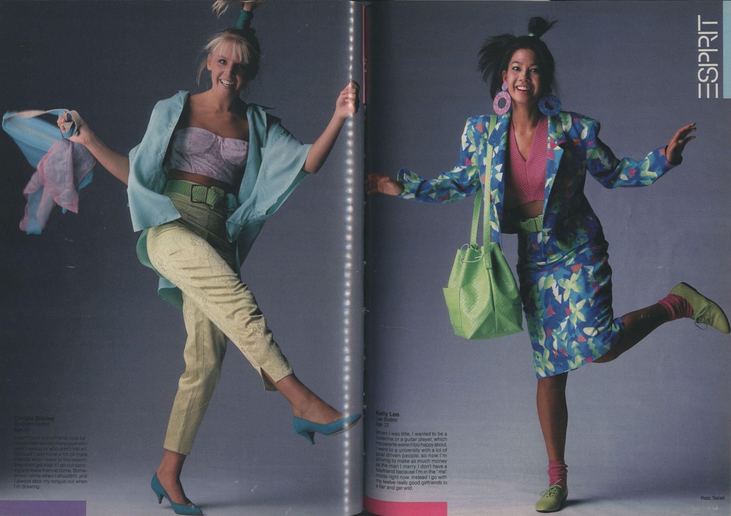 Two women in bright, colorful 1980s outfits pose energetically against a plain backdrop. One wears pastel pants with a blazer, the other a vibrant floral skirt suit, both accessorized with bold jewelry and bags.