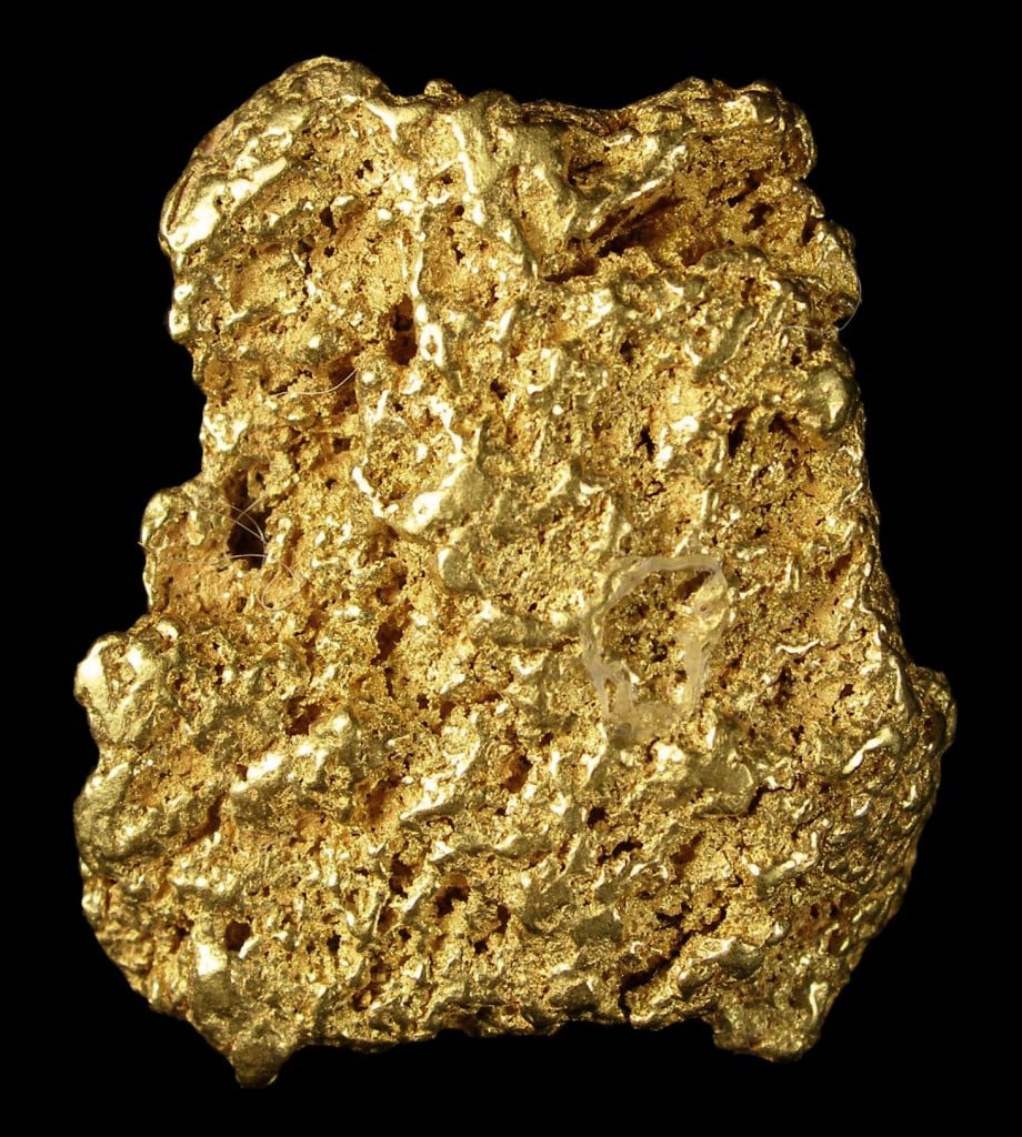 A close-up of a rough, irregularly shaped gold nugget with a shiny, textured surface, set against a solid black background.