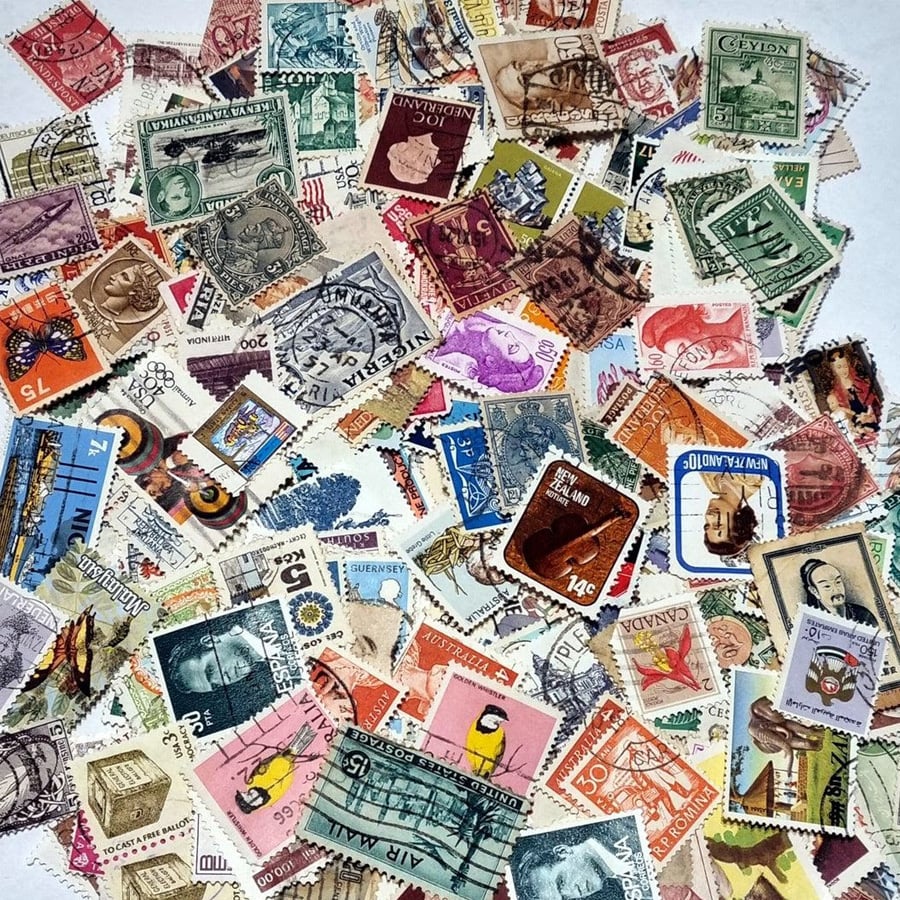 A colorful assortment of vintage postage stamps from various countries, featuring different designs, images, and denominations, scattered randomly on a white surface.